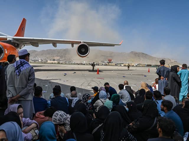 Afghan people sit as they wait to leave the Kabul airport. Photo by Wakil Kohsar / AFP via Getty Images