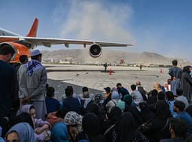 Afghan people sit as they wait to leave the Kabul airport. Photo by Wakil Kohsar / AFP via Getty Images