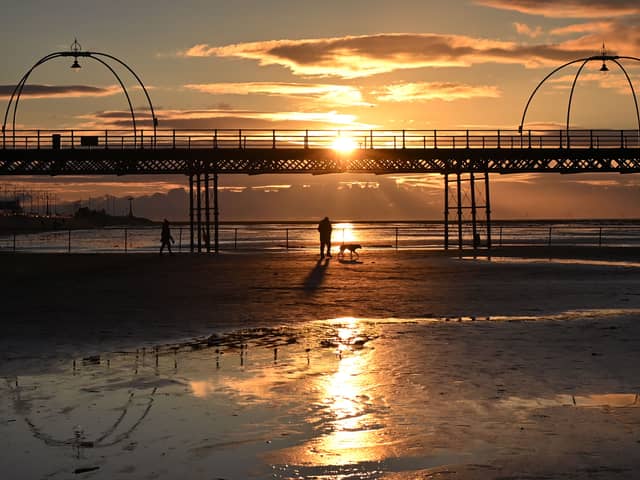 People walk with a dog along the beach at sunset, near Southport Pier. Image: PAUL ELLIS/AFP via Getty Images