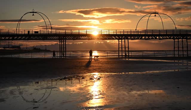<p>People walk with a dog along the beach at sunset, near Southport Pier. Image: PAUL ELLIS/AFP via Getty Images</p>