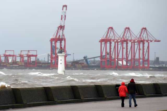 People walk along the promenade as waves crest in the mouth of the River Mersey.