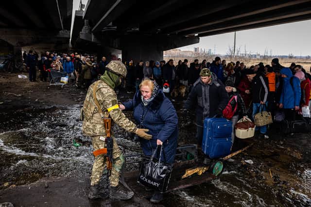 A Ukrainian serviceman helps evacuees gathered under a destroyed bridge. Image: DIMITAR DILKOFF/AFP via Getty Images
