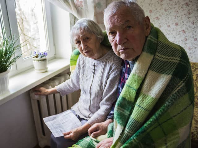 A senior man and woman holding a heating bill in front of a radiator.