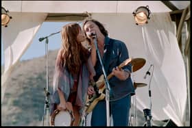 Riley Keough as Daisy Jones and Sam Claflin as Billy Dunne in Daisy Jones & The Six, singing into a shared microphone (Credit: Lacey Terrell/Prime Video)