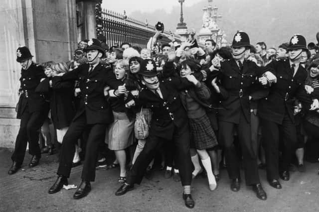 Police keeping back a crowd of young fans outside Buckingham Palace, London, as pop group the Beatles receive their MBEs.  (Photo by Ted West/Central Press/Hulton Archive/Getty Images)
