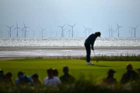 Wind turbines at the Burbo Bank Offshore windfarm are pictured on the horizon as England's Tommy Fleetwood putts on the 13th green