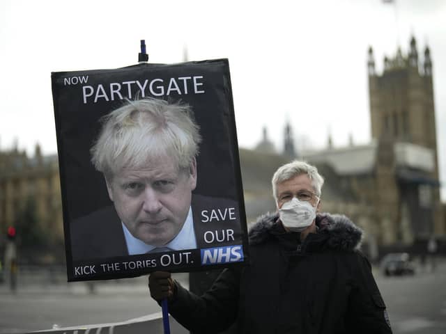A protester holds a placard with an image of British Prime Minister Boris Johnson including the words "Now Partygate" backdropped by the Houses of Parliament